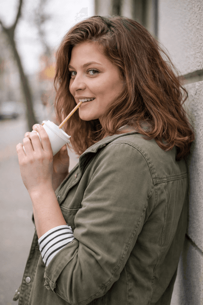Mujer sonriente bebiendo con pajita en la ciudad, succión oral funcional
